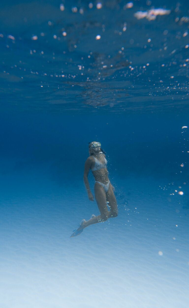 Full body of anonymous lady in swimsuit and flippers with snorkeling mask swimming undersea in clear blue water