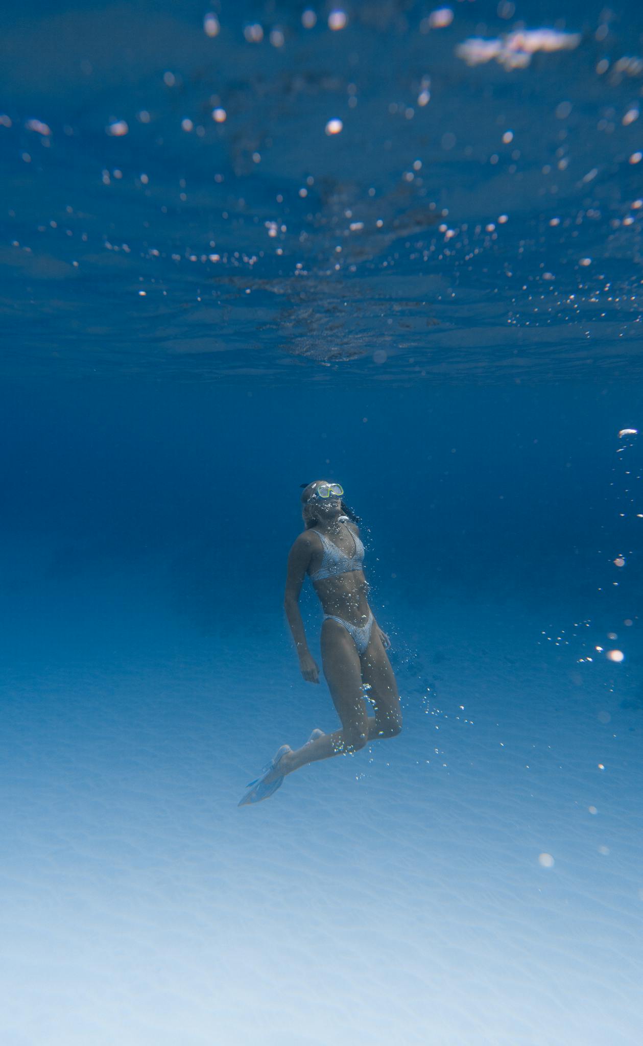 Full body of anonymous lady in swimsuit and flippers with snorkeling mask swimming undersea in clear blue water